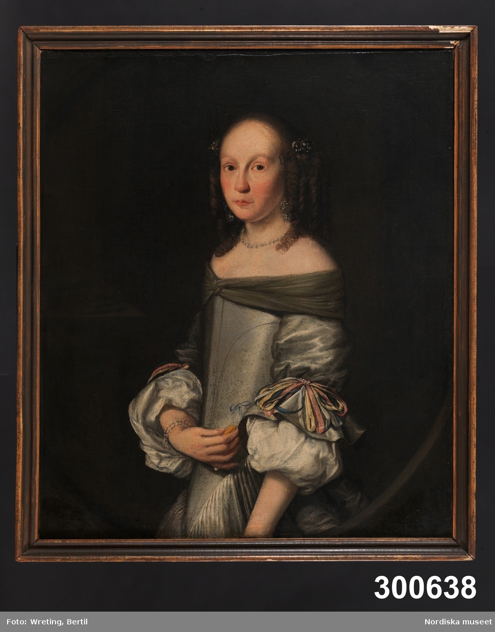 Porträtt av ung kvinna, midjebild fas vänster. Mörkbrunt hår med korkskruvslockar, gråvit sidenklänning med åtsittande liv.