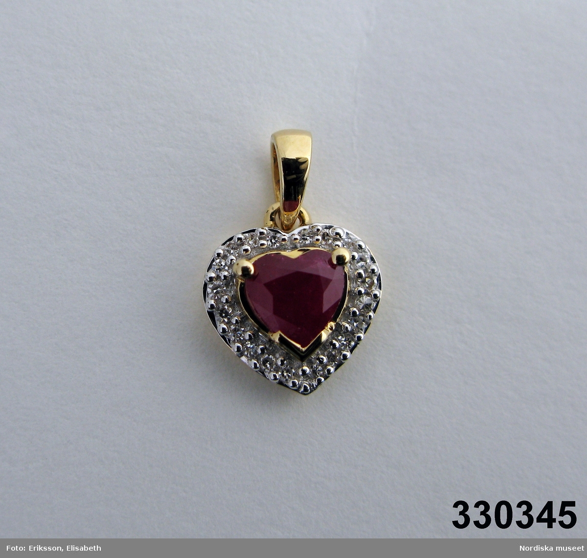 Hänge i form av ett hjärta. Tillverkad av rött guld med en hjärtformad facettslipad rubin i mitten omgjärdad av 36 st diamanter. Ädelstensvikten är för rubinen 0,61 ct och för diamanterna 0,108 ct.
Ingrid Roos 2010-03-04