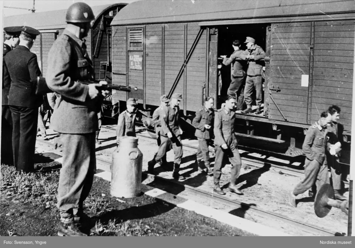 Tyska soldater på svensk järnvägsstation bevakas av svensk militär, troligen krigsfångar på väg tillbaka till Tyskland efter krigsslutet 1945.