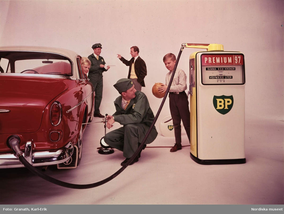 Reklambild med bensinpump, för BP, tagen i studio. Familj tankar en röd och vit Volvo Amazon och får trycket i däcken kontrollerade.