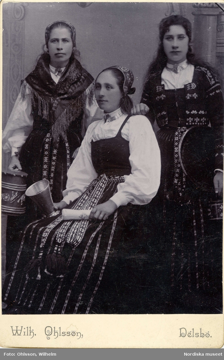 Tre unga kvinnor i folkdräkter. Alla tre klädda i dräkter från Delsbo, Hälsingland.