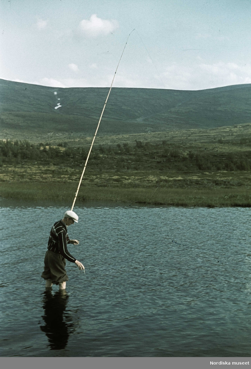 Landskap med en man som fiskar. I bakgrunden fjäll.