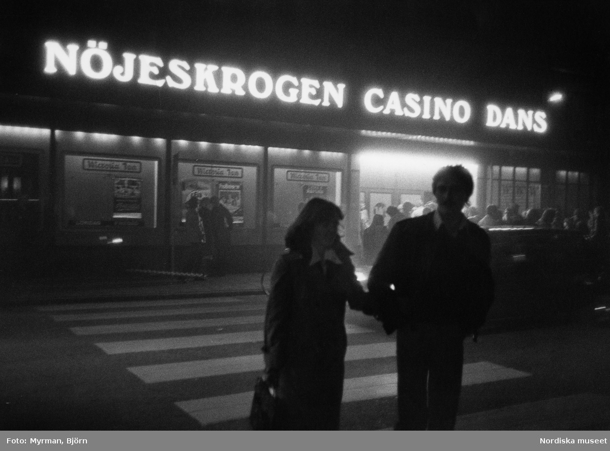 Entré till restaurang "Nöjeskrogen Casino Dans". Kvällsbild, i förgrunden ett par, kvinna och man, i bakgrunden människor i kö till restaurangen.
