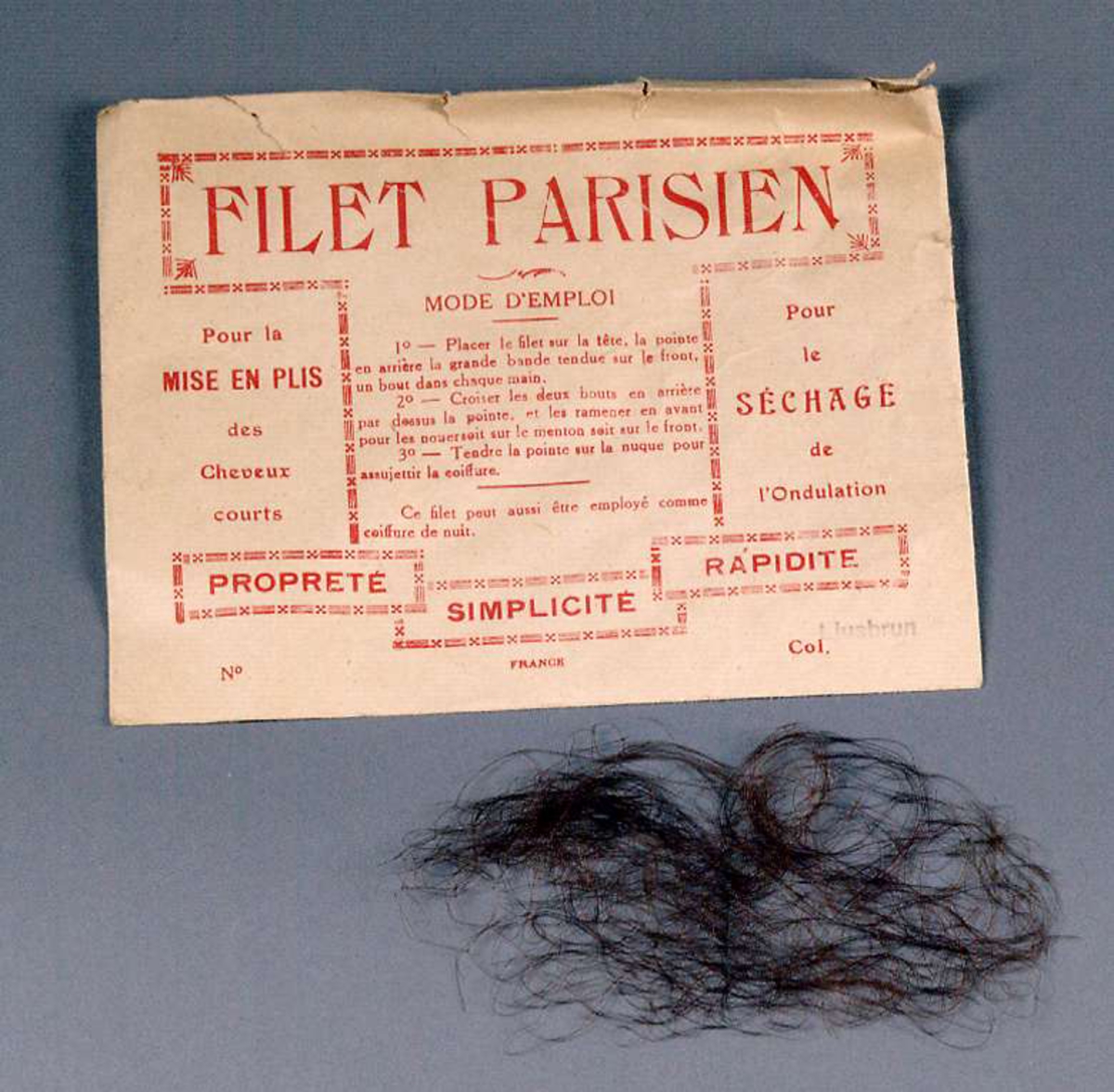 Ett hårnät av äkta hår i sin originalförpackning, ett kuvert med röd text: FILET PARISIEN MODE D´EMPLOI.