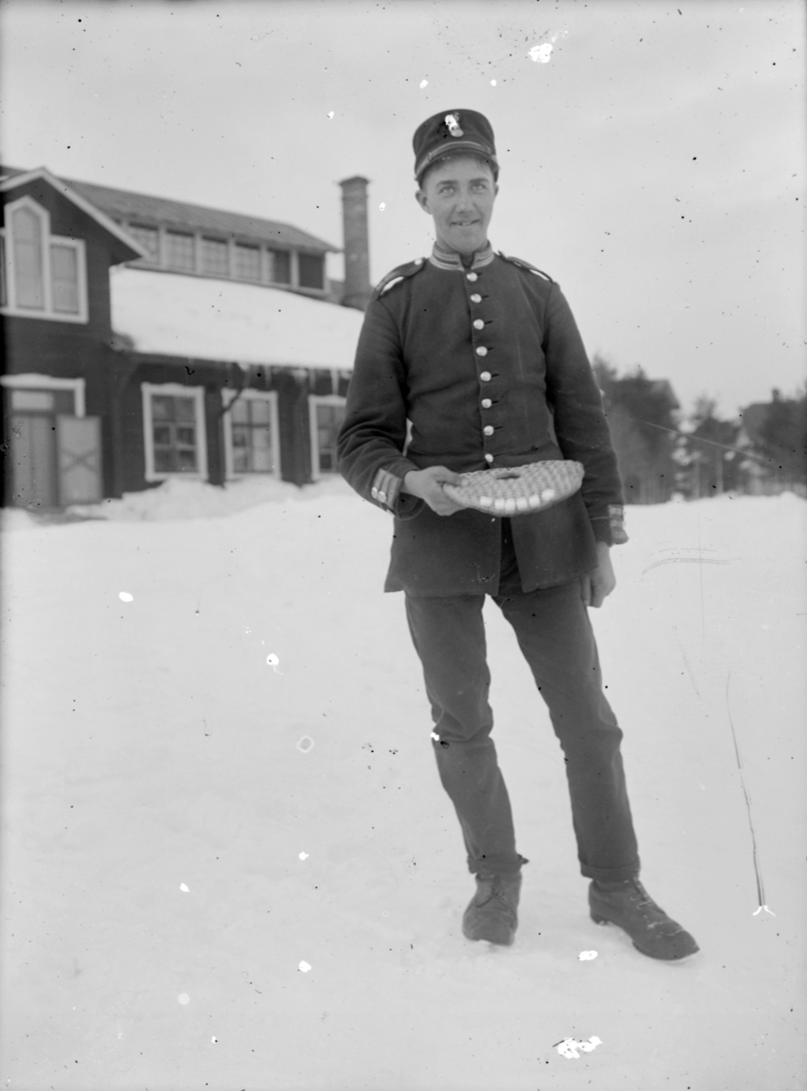 En armésoldat från I 4 eller I 5 regemente står med en brödkaka i handen på Malmens lägerområde, vintertid.