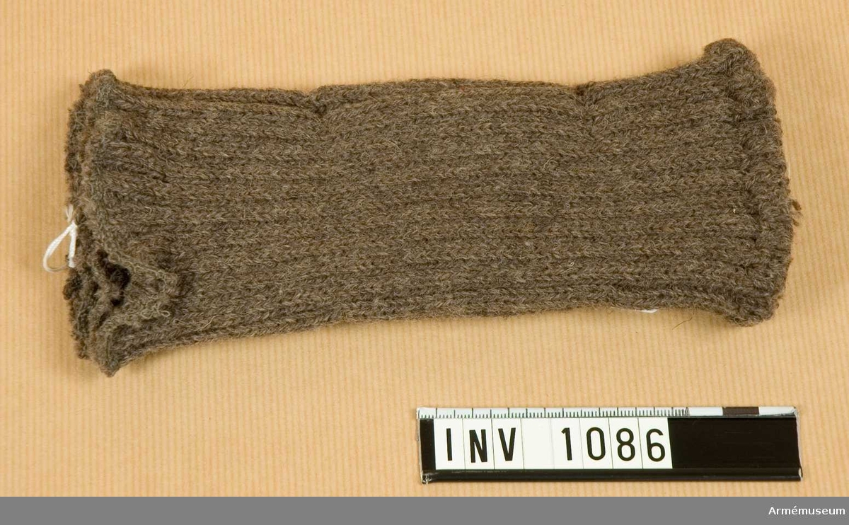 Maskinstickad av gråbrungrönt yllegarn i resårstickning. Tjugo mm från ena kanten är den öppna kanten ihopfästad, vilket bildar ett stopp för tummen när handen träs in.

Samhörande nr är 1074-1129, 8240, (1086-1087).