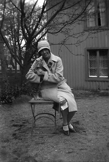 Maj Berggren sitter på en trädgårdsstol med en katt i famnen