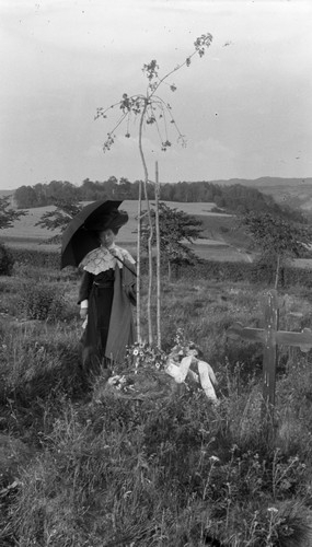 Kvinna vid grav på Foss kyrkogård. Troligtvis är det en nyplanterat sorgträd vid gravvården