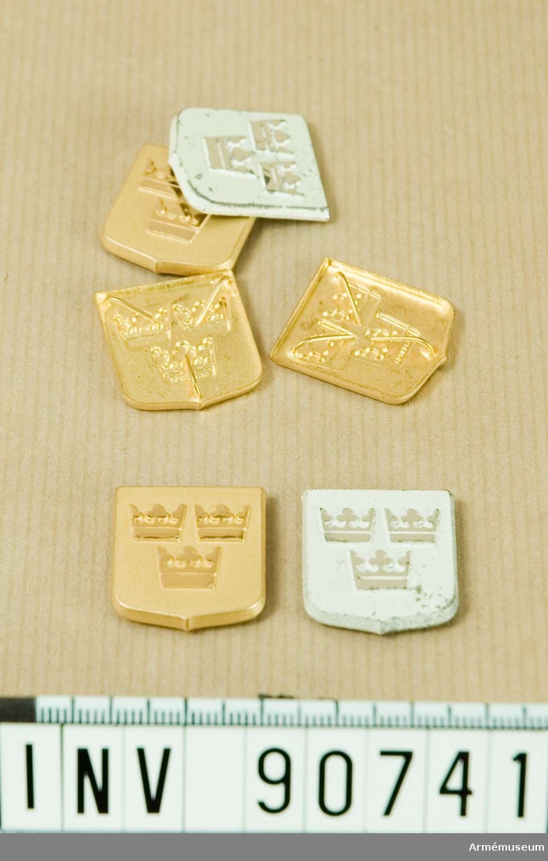 Låda innehållande fyra guldfärgade och två vitmålade märken föreställande tre kronor.