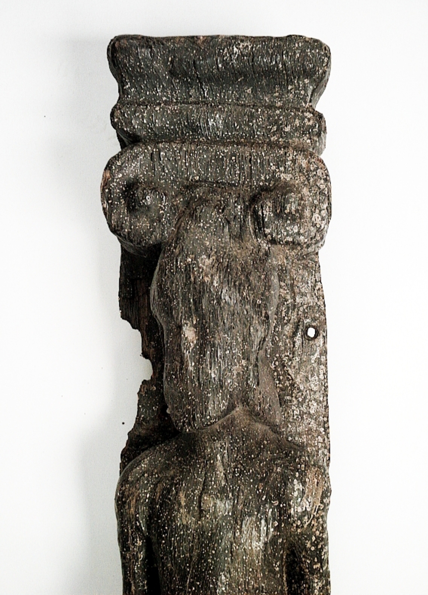 Pilaster föreställande en naken herm under joniskt kapitäl.
Hermen är iförd en stor hjälm. Huvudet är vridet åt höger.
Nedtill är pilastern prydd med en stor rullverksvolut och fruktornament. Fotändan har formen av en tunn, snedskuren och slät tapp eller tunga, med en något kilformad profil, som kan beskrivas som en fortsättning på bakstycket. Skulpturens baksidan är slät.
Skulpturen är relativt välbevarad. Ansiktsdragen är dock utplånade och händerna är bortnötta.

Text in English: Sculpted pilaster with naked Herm, under an Ionic capital.
The Herm is probably wearing a large helmet. The head is turned to the right.
The lower part of the pilaster is decorated with a large scroll-work volute and fruit ornamentation. The foot end is shaped as a thin, smooth, angled tenon (rather wedge-shaped in profile) that may be described as an extension of the backboard. The rear side is smooth or flat.
The sculpture is rather well preserved, but the features of the face obliterated and the hands are worn away.
