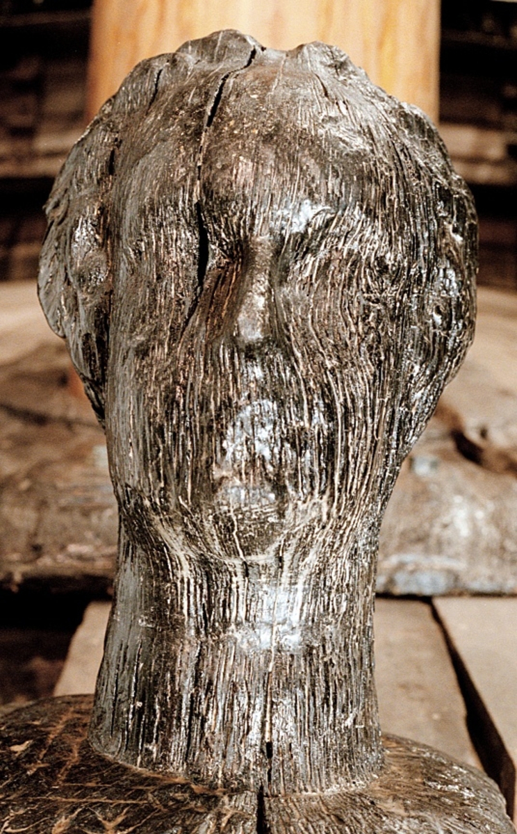 Rektangulär knekt med två skivgatt.
Upptill är knekten krönt med ett tredimensionellt kvinnohuvud med rak, klassisk profil och en konstrik frisyr av romerskt snitt. Huvudet är riktat föröver och snidat i ett med knekten. Runt halsen, på knektens ovansida, är antydan till en bred och platt spetskrage eller liknande. På knektens sidor finns märken efter stora järnbeslag.
Skulpturen är ytsliten men relativt välbevarad.

Text in English: A rectangular knight with two sheave holes.
On top of the knight is a three-dimensional female head with a straight, classical profile and an artistic coiffure of Roman style. The head is carved as part of the knight and faces the bow. Around the neck, on the upper end of the knight, there is a suggestion of a broad flat lace collar or the like. The sides of the knight have marks for large iron fittings.
The sculpture is relatively well preserved despite the worn surface.