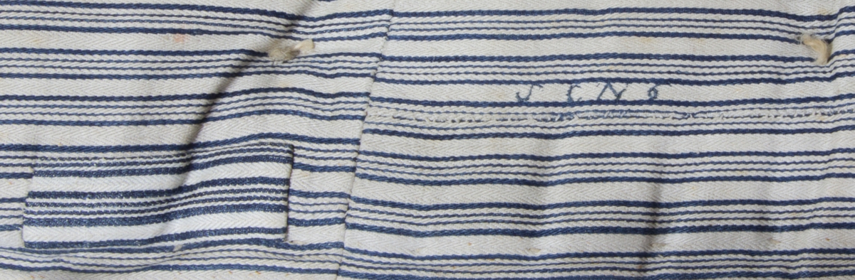Madrass, tillverkad av troligen handvävt linnetyg, spetskypert. Varp randig i blått och vitt, inslag vitt. Puskor knutna av en ensam hamptråd. 
Märkt med blå tråd: S C N 6 på två ställen. 
Fyllning: gräs.