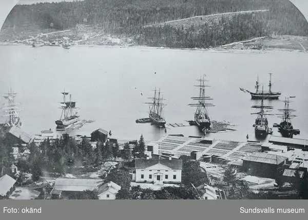 I förgrunden Svartviks herrgård i bildens mitt  hamnområdet med magasinbyggnader och uppläggningsplatser för timmer, i vattnet ligger cirka sju segelfartyg.