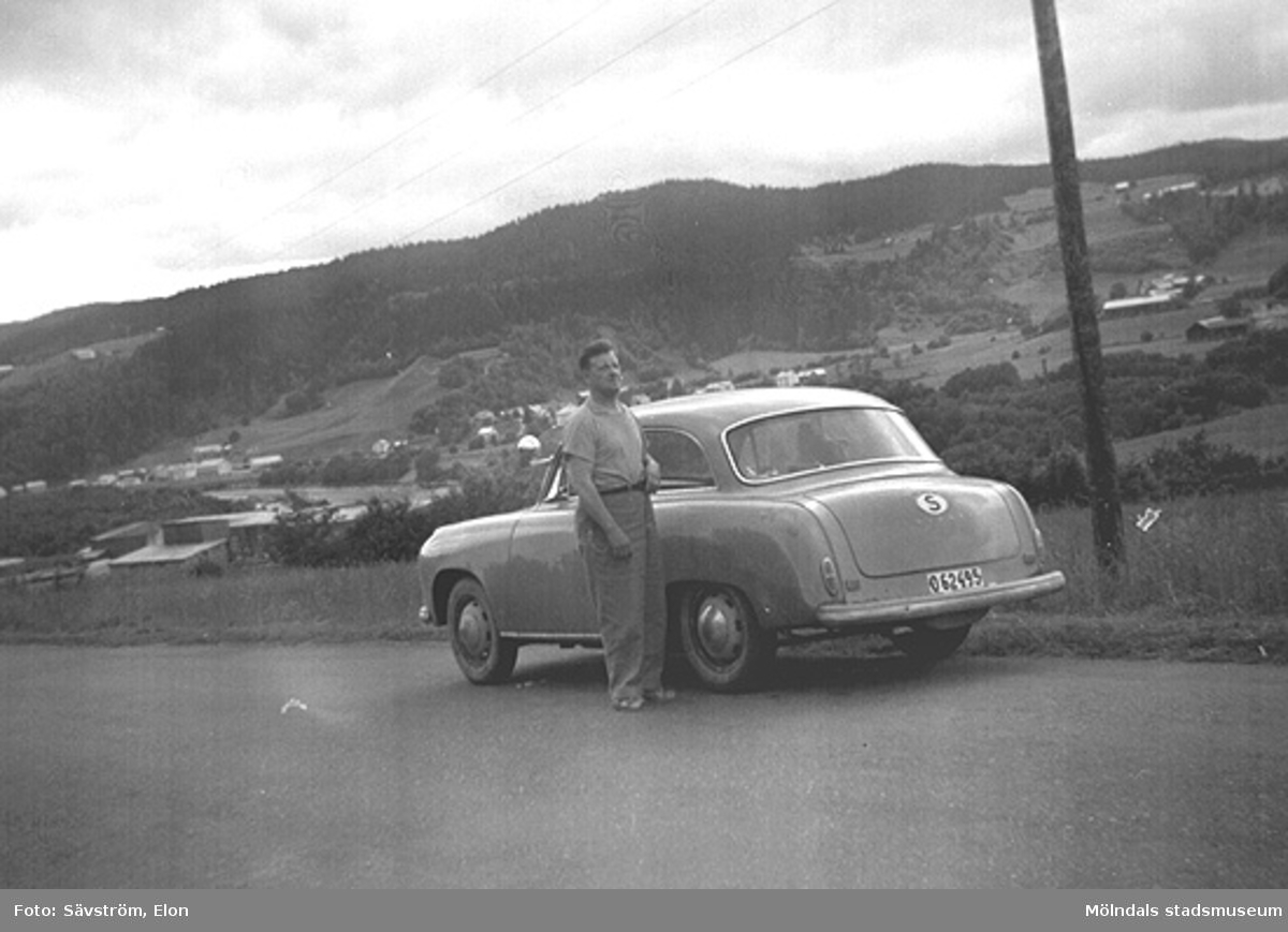 Helmer Garthman är på väg till Norge för fiskesemester med Elon Sävström och dennes bil, en Goliat Isabella. Här är det paus i Värmland. 1960-tal. Skänkt av sonen Alf Garthman som arbetade många år på Mölndals stadsmuseum.
