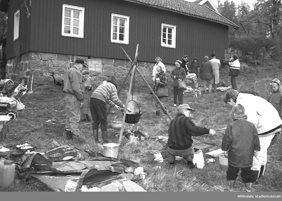 Familjesöndag vid Börjesgården, 1994-05-15. Besökare ser på när Museichef Mari-Louise Olsson kokar soppa över öppen eld. Sittandes på huk är museitekniker Alf Garthman.