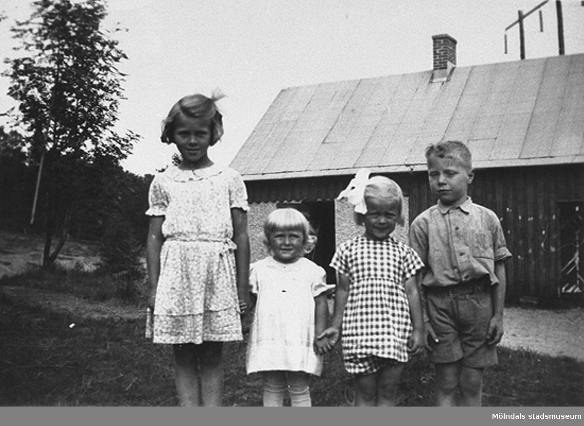Sommar i Lindome, början av 1940-talet. Fyra barn poserar framför kameran. I bakgrunden ses en lada.