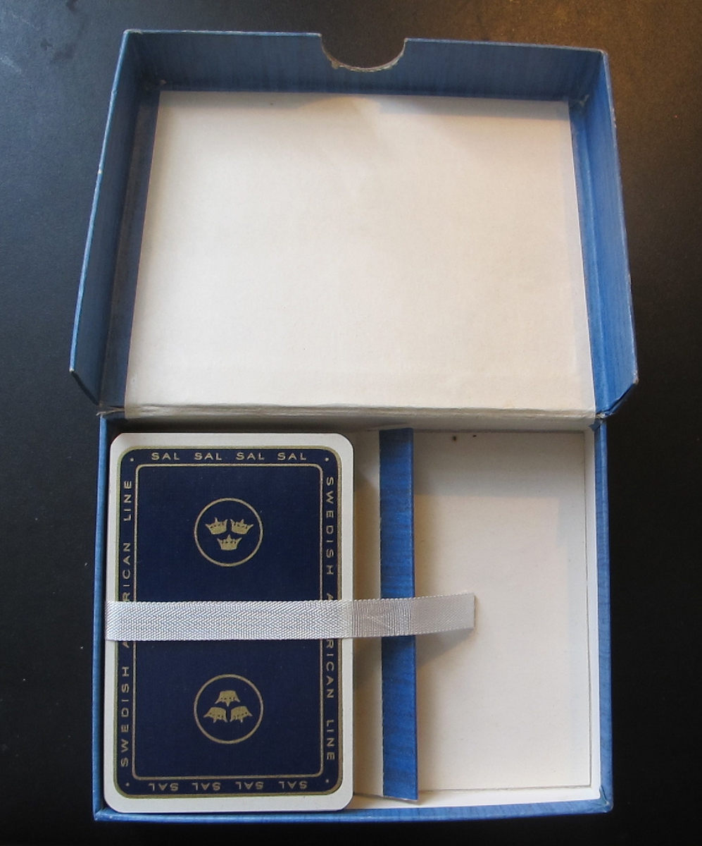 En komplett lek spelkort i ask. Kortens baksida blå med SAL:s emblem med tre kronor och bord med "SAL" i guldtryck. Asken blåmelerad med vitt foder, vitt sidenband för kortlekens placering, rött och blått spelkoert på askensundersida.Föremålets form: Rektangulärt