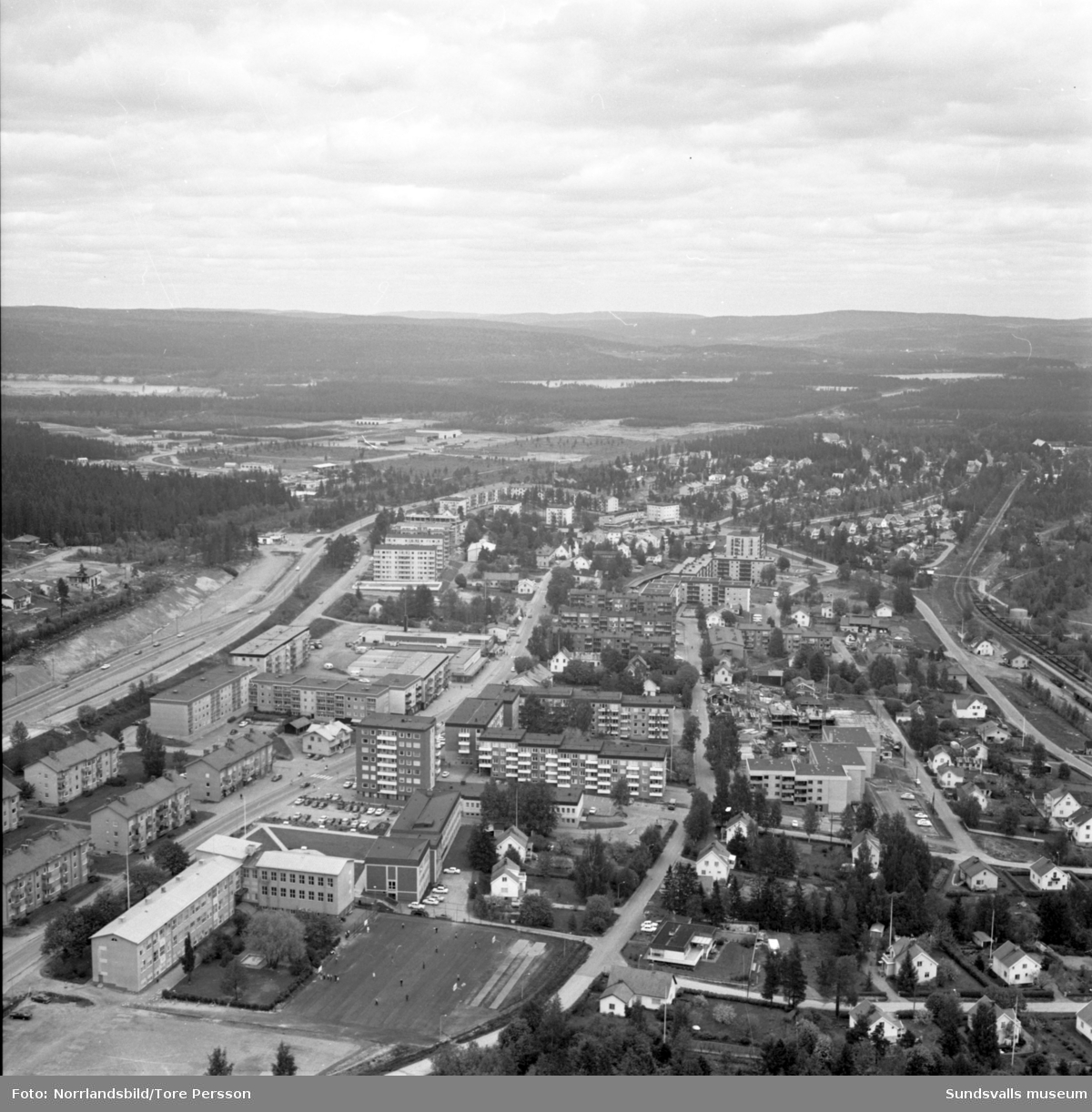 Flygfoton över Timrå med omnejd. Centrum, industriområdet, idrottsplatsen med "Grytan" och isladan, Östrandsfabriken, Vivstavarvstjärn, landsbygd.
