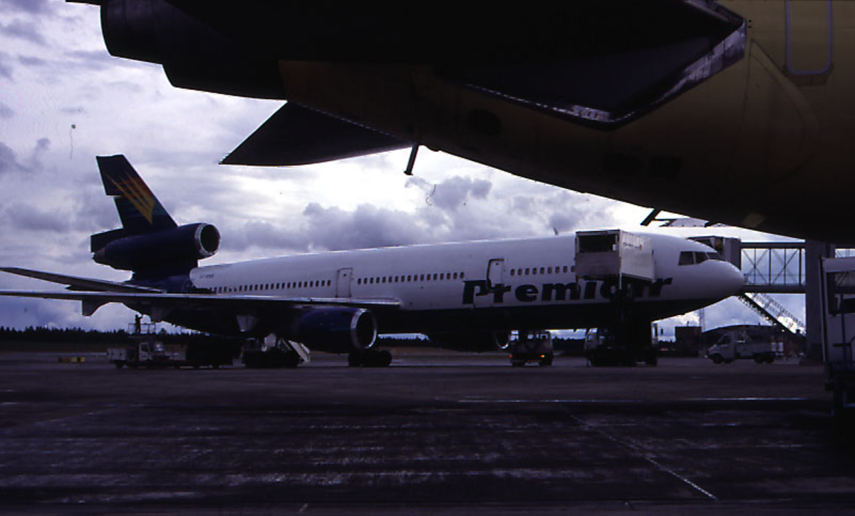 Luftfart, 1 fly på bakken ved terminalbygningen, DC-10, OY-CNS fra Premiair.  Landgangen og 4 kjøretøyer rundt flyet.  Buken til 1 annet fly i forgrunnen.