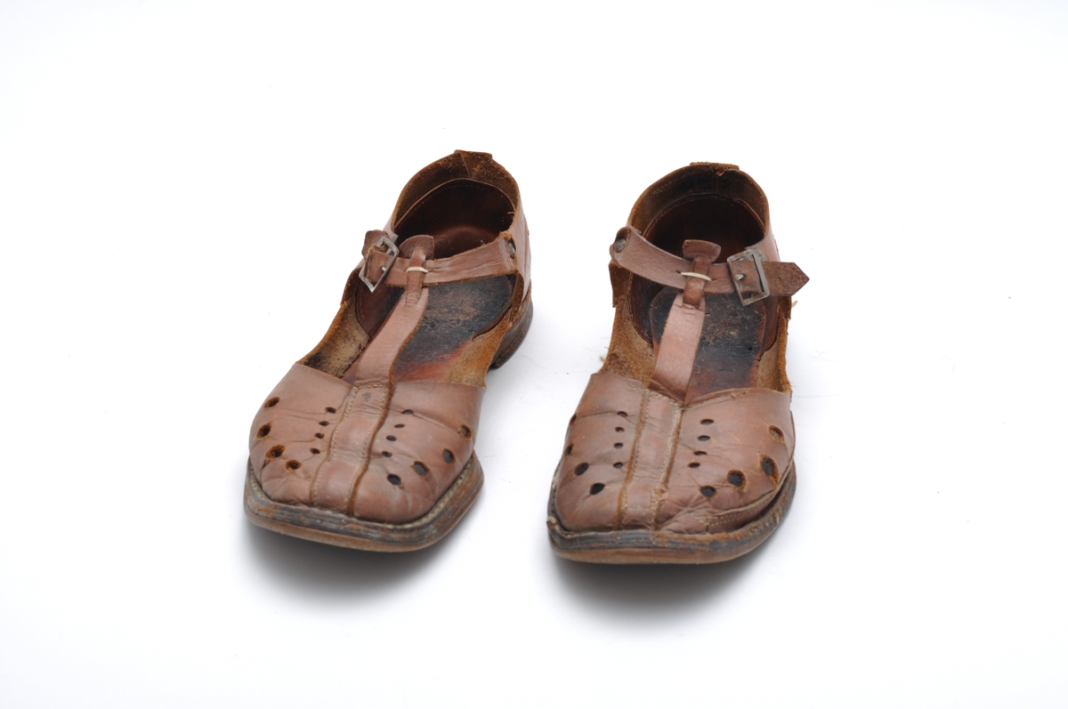 Sandal i brunt naturfarget lær. Lav hæl, reim og spenne. Velbrukt. Dekortivt hullmønster i overlær.