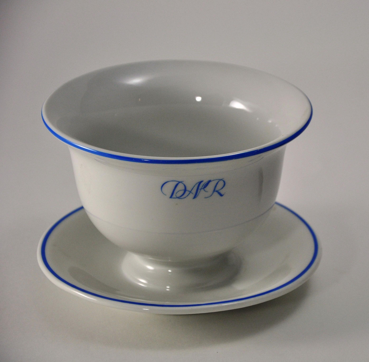 Sausebolle på skål i hvit porselen. A/S Den Norske Reiseeffektfabriks initialer "DNR" og munningsrand er påmalt i blått.