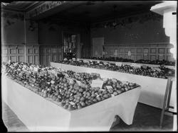 Interiør fra utstilling av frukt i en stor sal.
Plakat på v