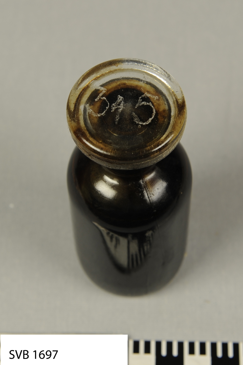 Glassflaske med tykk sort væske. Det er håndskrevete tall på lokken og flaskekroppen.