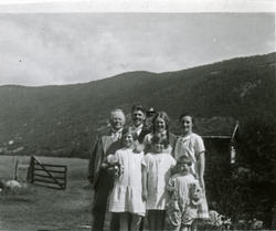 En kvinne, to menn og fire jenter står ved et gjerde. Innenf