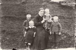 En kvinne i sort kjole m/ hvit krage, sammen med fire barn f