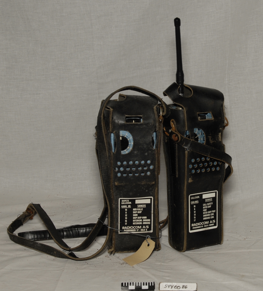 Betegnelse:VHF-samband
To rektangulære apparater med lærhylster og bærereim. Det er en antenne på den ene apparatet.