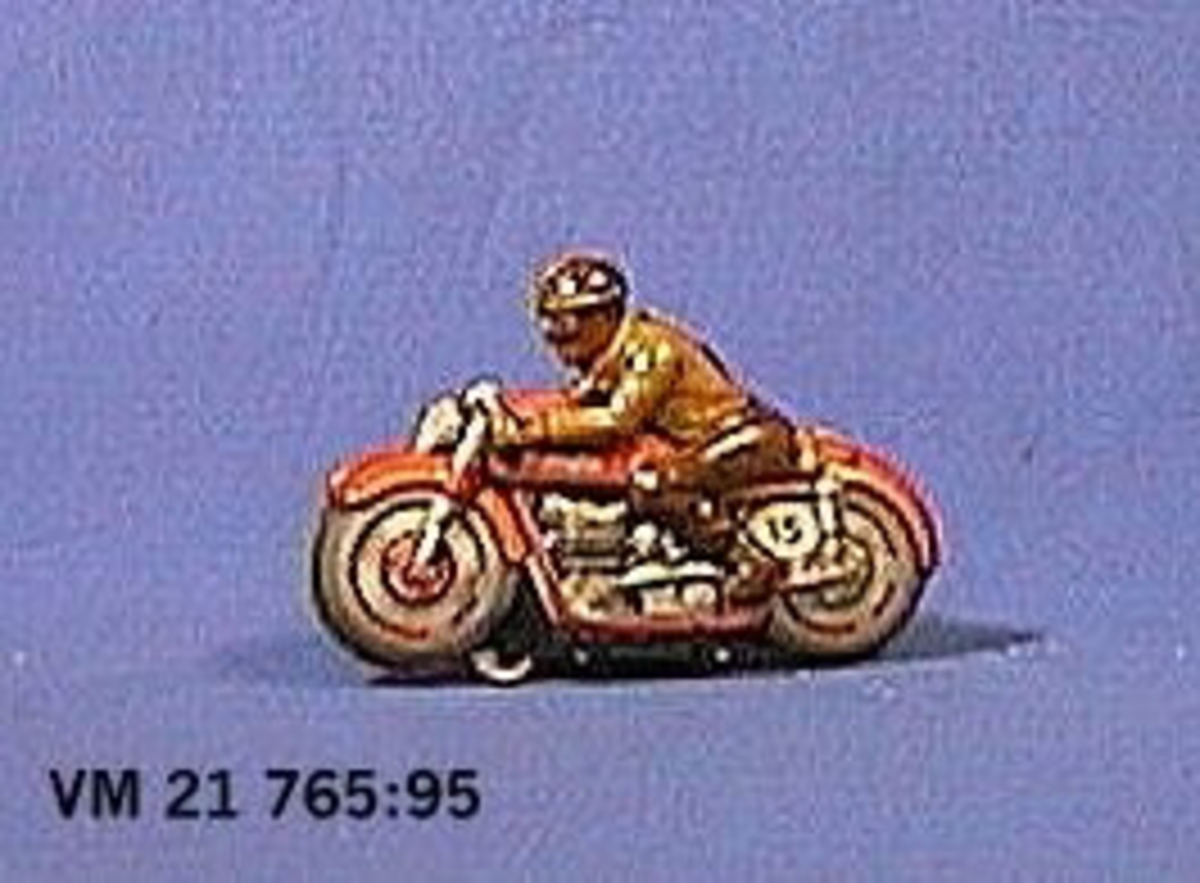 En motorcykel med förare tillverkad av litograferad plåt. Drivhjul saknas. Tillverkad i U.S.-Zone i Väst-Tyskland. L. 18,2 cm.  H. 12 cm.  B. 3,1 cm.