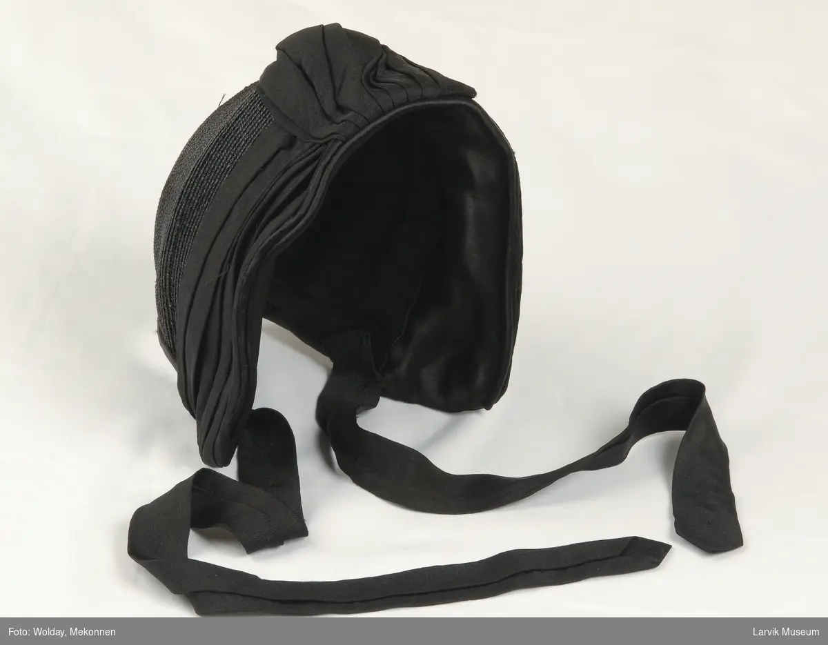 Form: liten kyse fasong, Besetning i forkant med draperi midt foran av sort krypert silkestoff noen går over i knytebånd.
