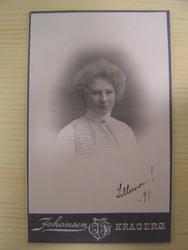 Dame m/ oppsatt hår, hvit bluse m/ lite smykke i halsen.