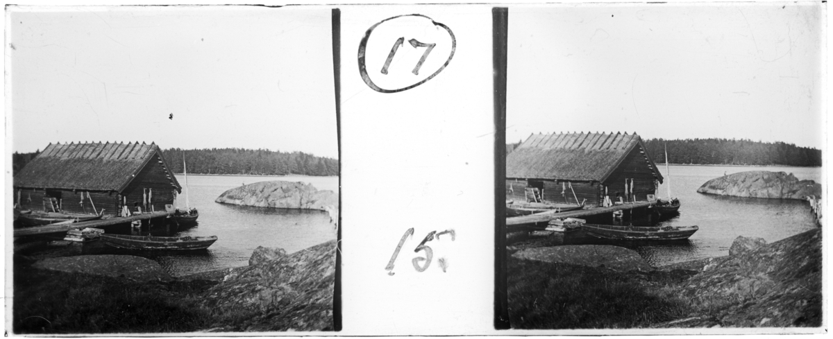 'Bildtext: ''Landing stage at Säfö.'' (Landningsplatsen vid Säfö) :: Vy med 1 båtskjul,timrat  trähus, liggande nere vid vattnet med brygga och i vattnet ekor. I en båt sitter 1 person. PÅ väggen till byggnaden hänger ev. nät. ::  :: Ingår i serie med fotonr. 5251:1-21, se även hela serien med fotonr. 5237-5267.'