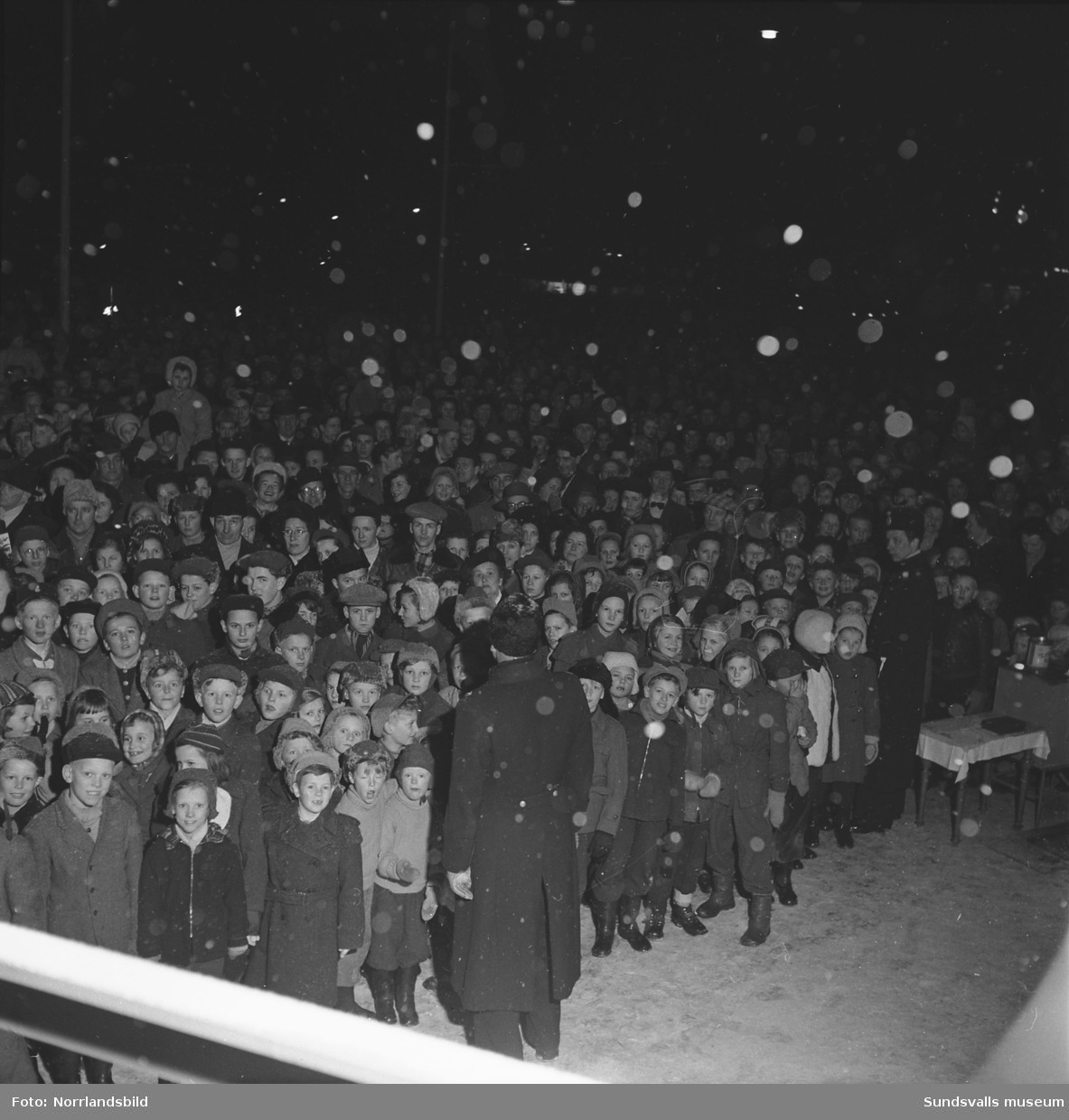 Högtidlig invigningsceremoni av Svenska skidspelens på Stora torget i Sundsvall. Snön faller och torget är fullpackat av folk.