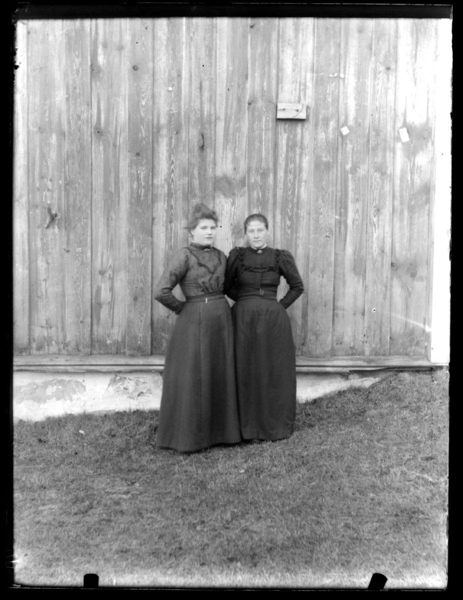 To ukjente kvinner stående mot en husvegg
