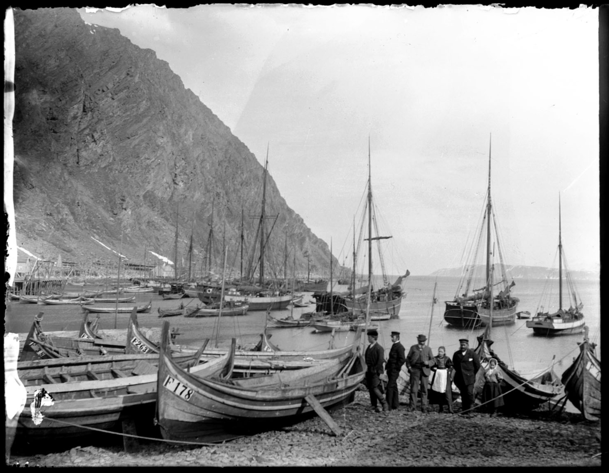 Båter dratt opp i fjæra i Finnkongkeila. Fire menn, to (unge) damer poserer for kamera. Vi ser registreringsnummer på mange av båtene: F 178, F 263, F 38.