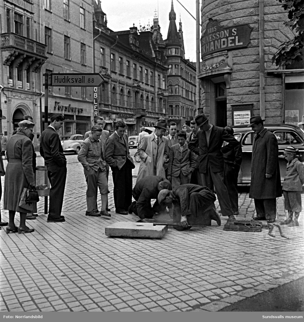 Ett par gatuarbetare som åtgärdar någonting i hörnet av Storgatan och Bankgatan, mitt för Sunessons bokhandel, väcker stort intresse bland de förbipasserande.