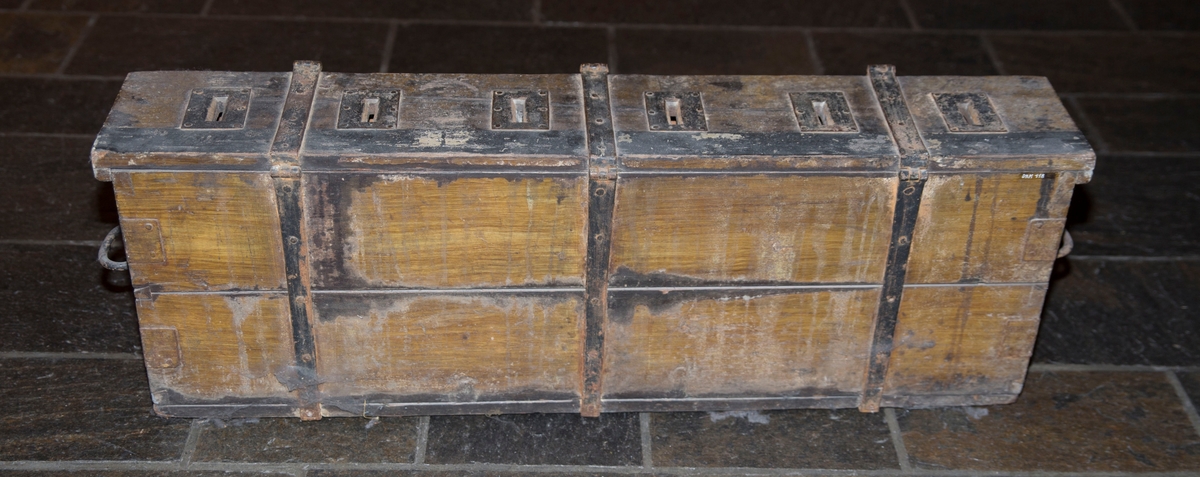 Lang smal kasse med lokk og jernbeslag. Den har tre fester til hengelås og håndtak på sidene.