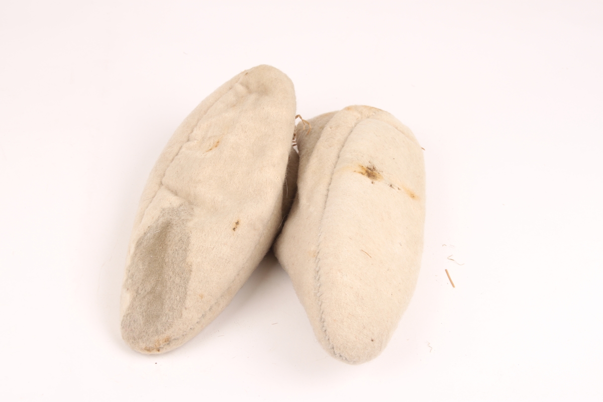 Et par hvite sokker i vevet ulltøy uten dekor. Sokkene stanser ved ankelen og er fylt med sennegress.