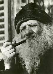 Portrett av en eldre mann med skjegg og lue som røyker pipe.
