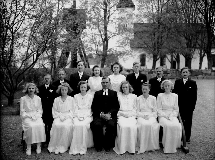 14 konfirmander, 8 flickor, 6 pojkar och kyrkoherde Gunnar Johanssonn, Biverud, Glanshammars socken.
Glanshammars kyrka och klockstapel i bakgrunden.