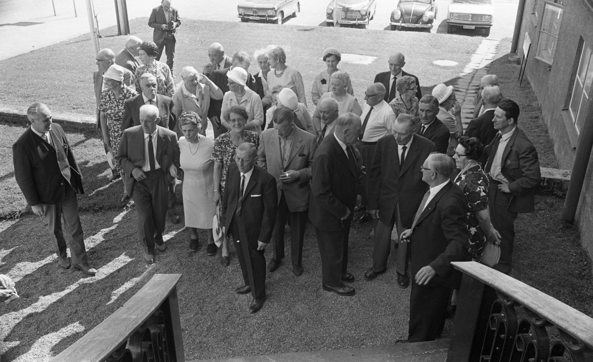 Grybe golf, Gustavsvik 17 juni 1967

En grupp äldre damer och herrar står samlade utomhus vid foten av en trappa. Många damer bär hattar och kappor. En del bär även hattar. Många män är klädda i mörka kostymer, skjortor och slipsar.