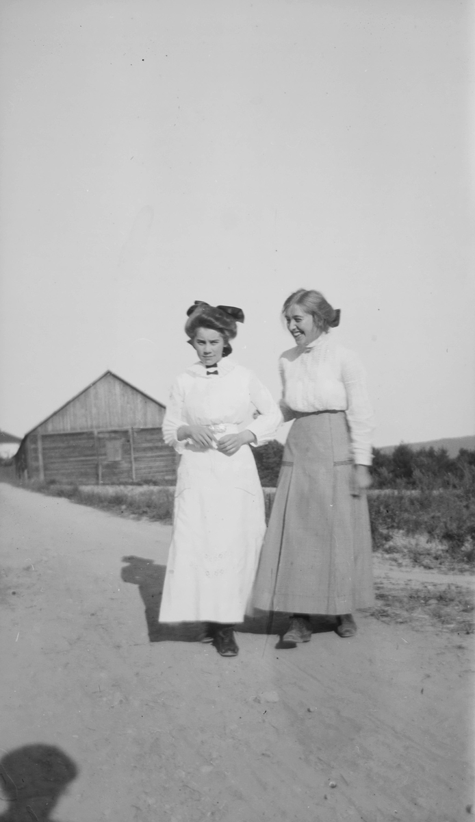 Celina Marie Mathiesen og en annen ung kvinne står på en grusvei i landlige omgivelser.