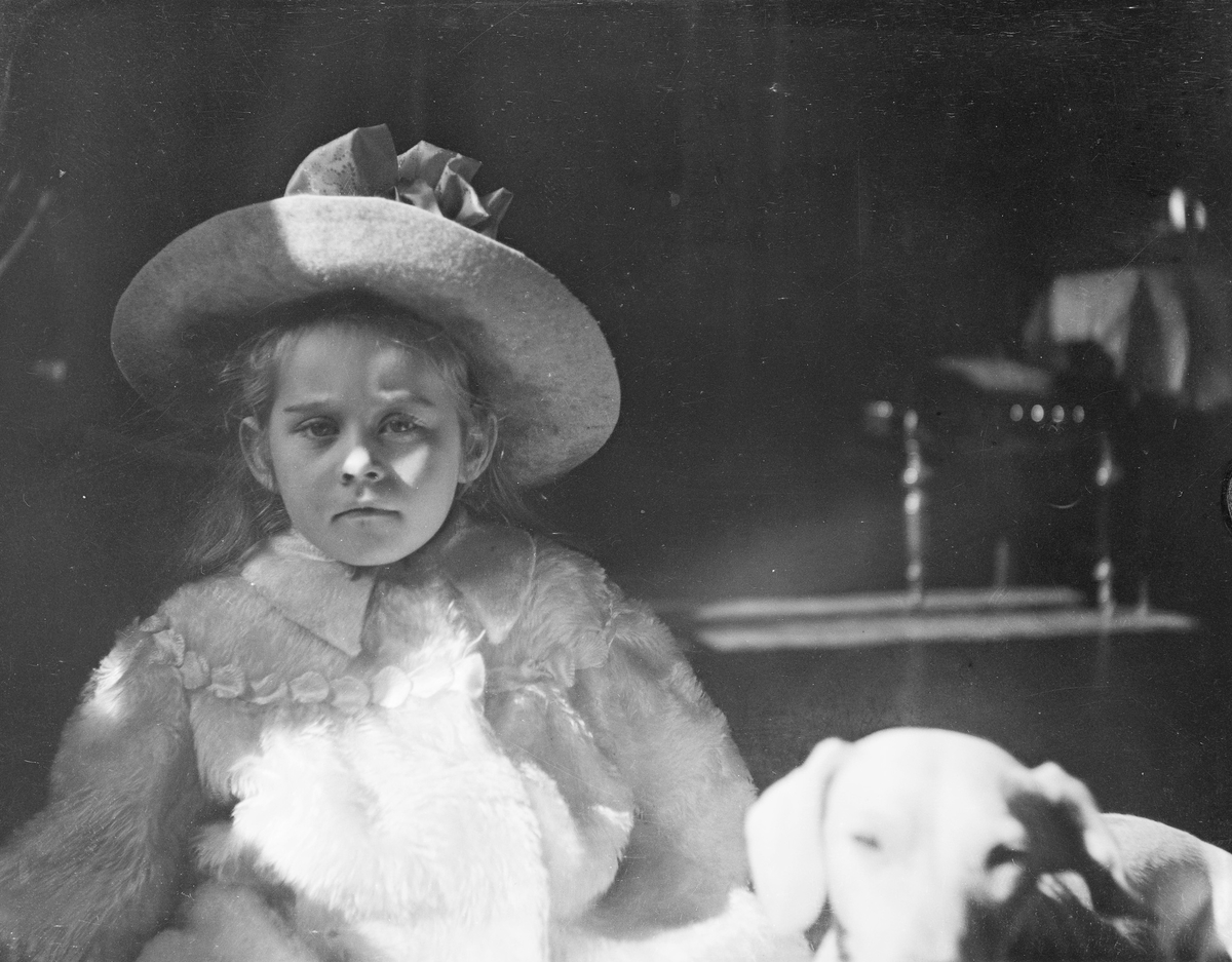 Ise (Louise) Mathiesen kledd i kåpe og hatt, sitter  med en hund ved siden av seg.