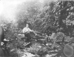 En mann sitter og fisker i elva.