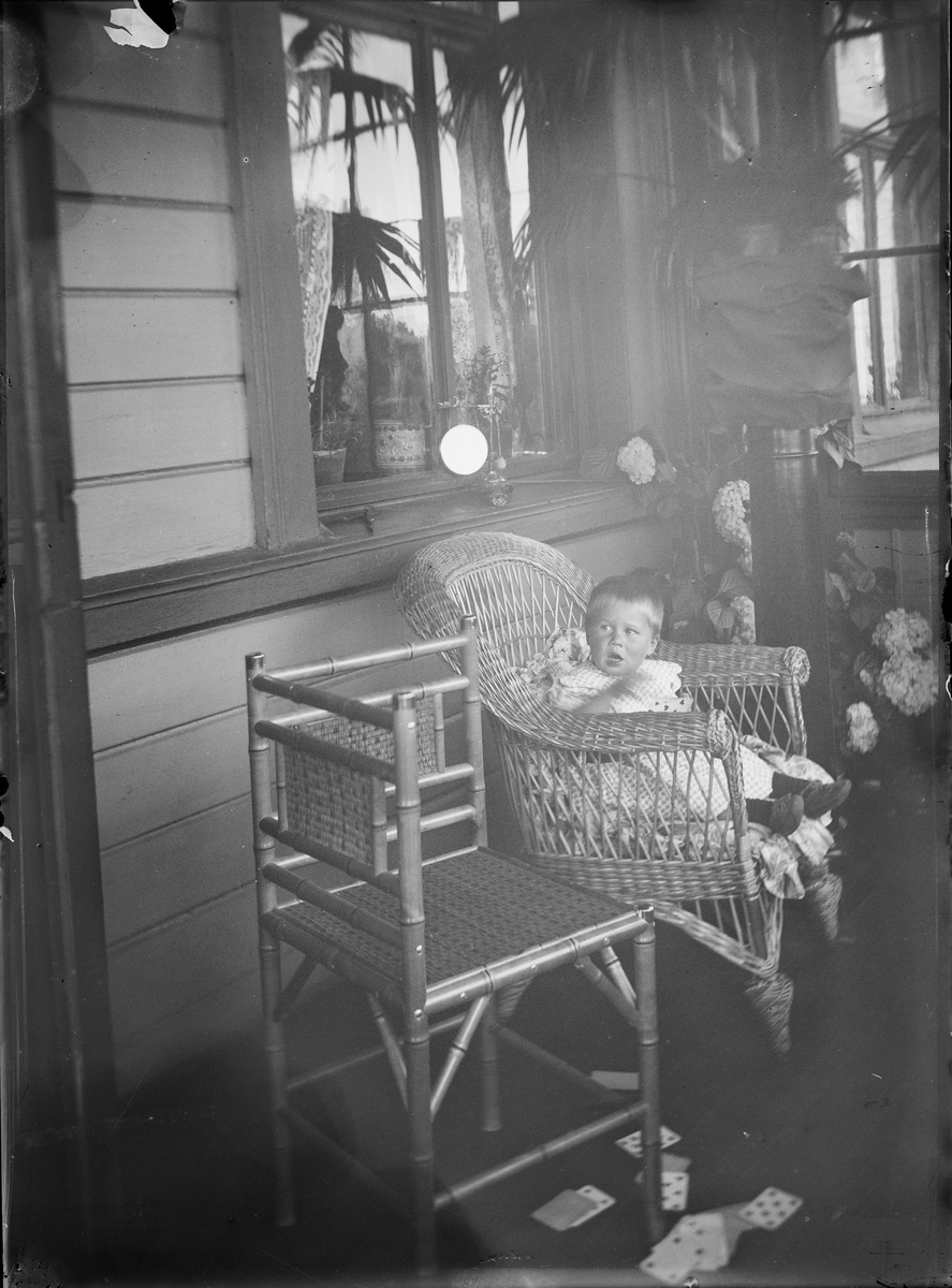 En gutt sitter i en kurvstol på en veranda. På bakken ligger en kortstokk.