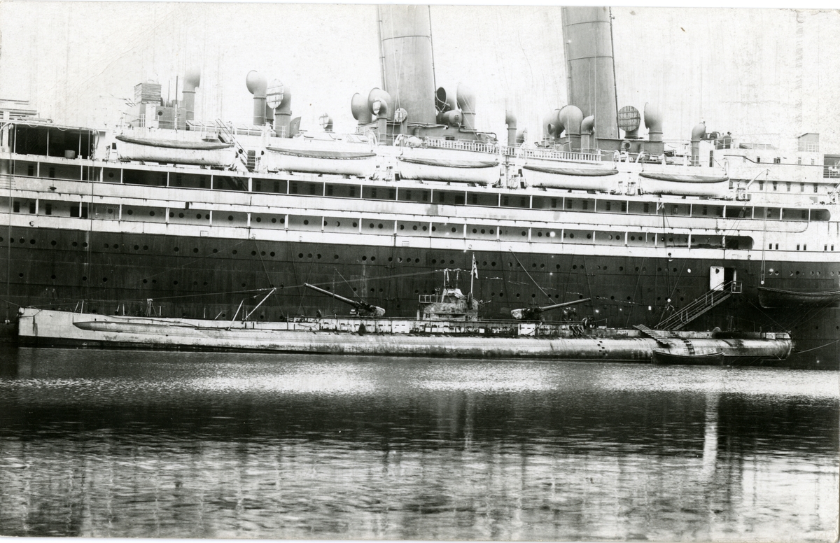 Torpedobåt ligger ved skipssiden til passasjerdamperen 'Berlin' som ble bygget for Norddeutscher Lloyd i 1909