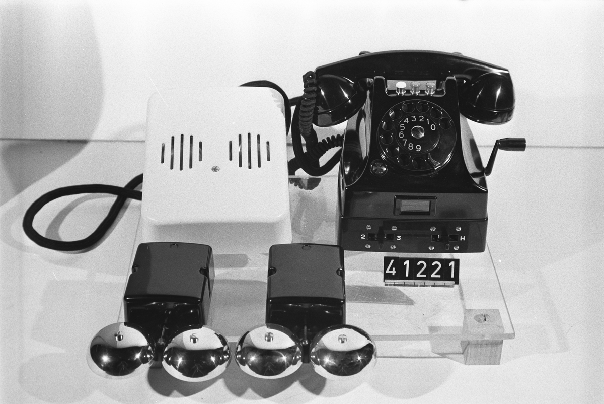 Telefonapparat BC 563 för AT-system, huvudapparat för två anknytningar av typ BC 562. Bordapparat modell m50 av svart bakelit med tre tryckknappar, vevinduktor, fastskruvad underdel av bakelit med två hävomkastare, två separata växelströmsklockor A0029506 och textilklätt apparatsnöre anslutet till väggplint A0029497 med vit huv och växelströmsklocka. Vikt: 5,2 + 1,1 kg.