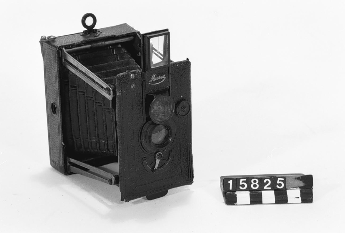 Klappkamera, bälgkamera för plåtar och plan-film 6 x 9 cm. Avståndsinställning genom olika linser på roterande skiva. Irisbländare på objektivet.